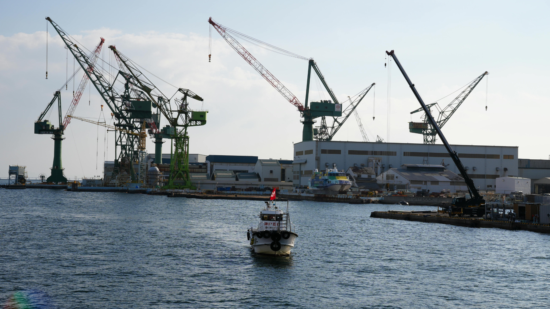 View of Kobe port featuring large cranes and a boat navigating the waters, ideal for industrial themes.